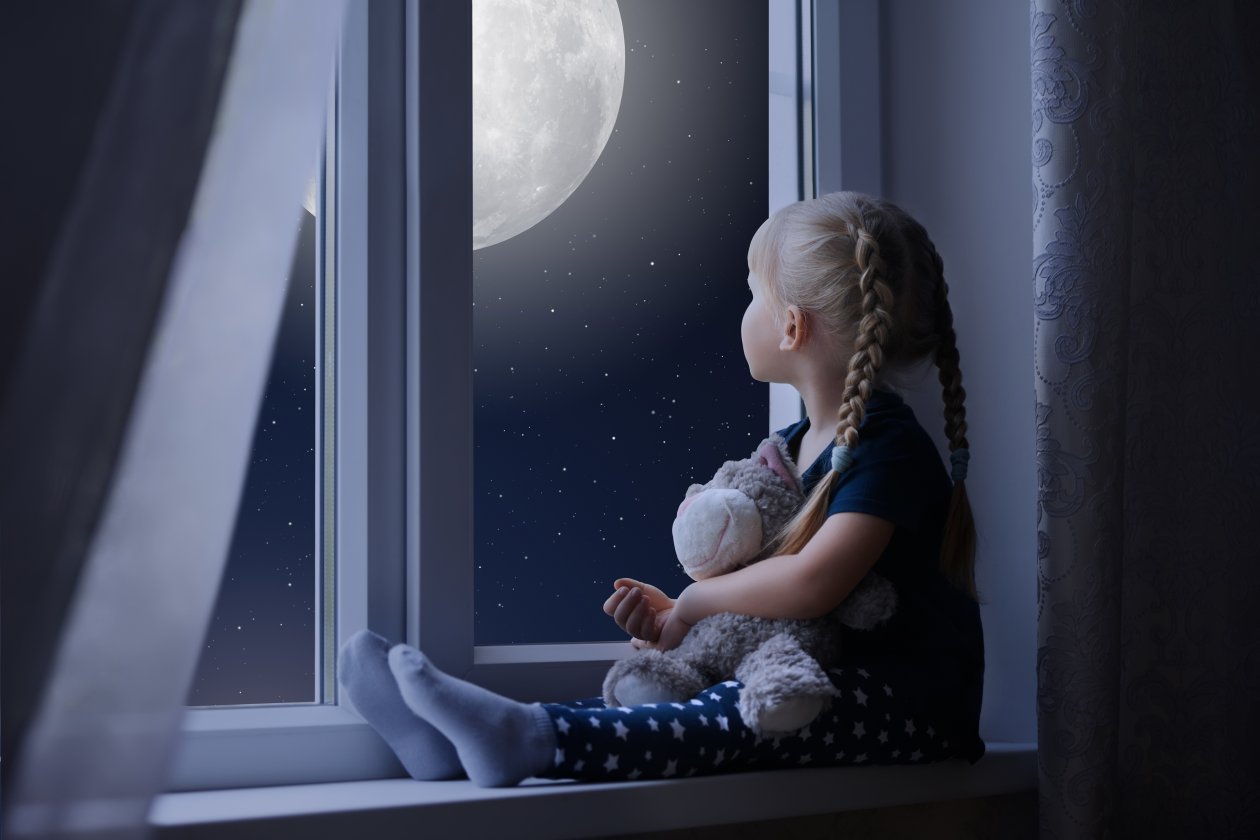 Little Girl Sadly Out Of A Window With A Teddy Bear