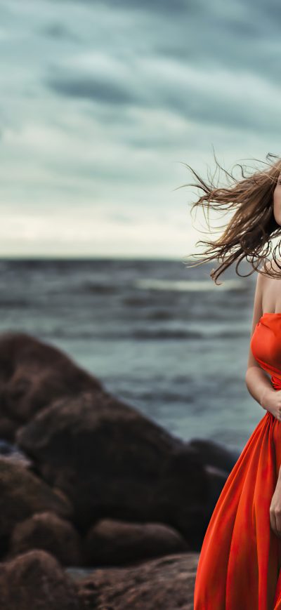 Fond d'écran iPhone Girl In Orange Dress Wind Blowing At Beach Rocks 4k