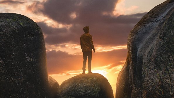Boy Standing On A Boulder In Between Mountains