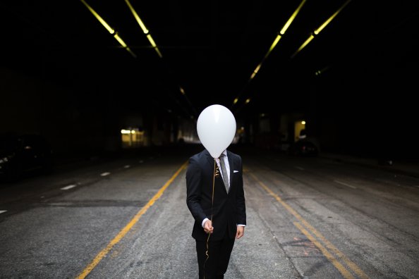 Young Man In Suit Holding Balloons In Front Of Face